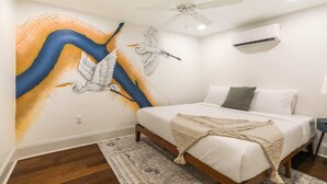 A bedroom with a bed, a ceiling fan, an air conditioning unit, and a wall mural.
