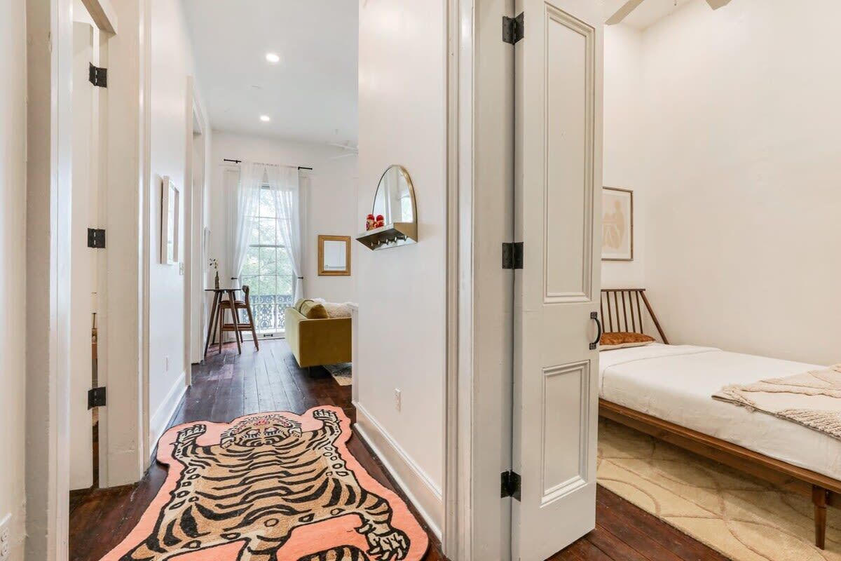 Un couloir orné d’un tapis à motifs de tigre mène à une chambre à coucher où se trouvent un lit et une fenêtre.