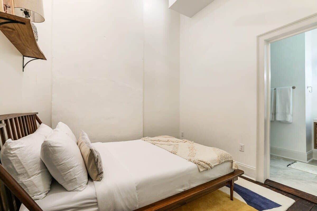 A small, neatly arranged bedroom with a single bed, a wooden headboard, and a light-colored wall.