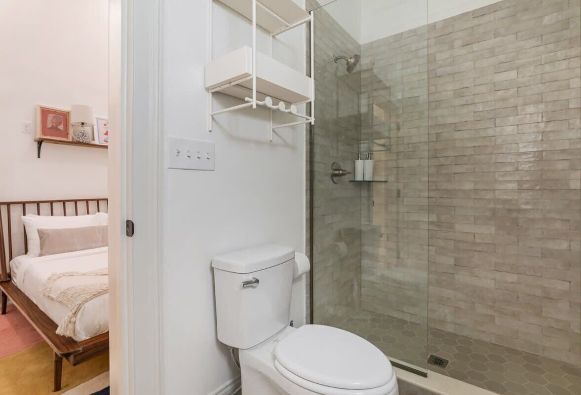 Un bagno con il water, una doccia con porta in vetro e un letto con testiera in legno.