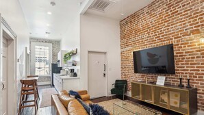 Ein modernes Wohnzimmer mit Backsteinwand, Flachbildfernseher, Ledersofa und Glastisch.