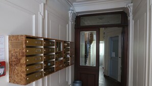A hallway with a row of metallic lockers on the left, a wooden door at the end, and a trash bin in the center. - Studio 10 m2 - Coeur Batignolles - Near Champs Elysées & Montmartre (Paris)