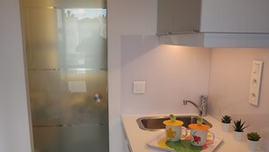 A modern kitchen with a stainless steel sink, a white countertop, and a small potted plant. - Studio 10 m2 - Coeur Batignolles - Near Champs Elysées & Montmartre (Paris)