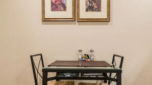A small dining area with a table and two chairs, framed pictures on the wall, and salt and pepper shakers on the table.