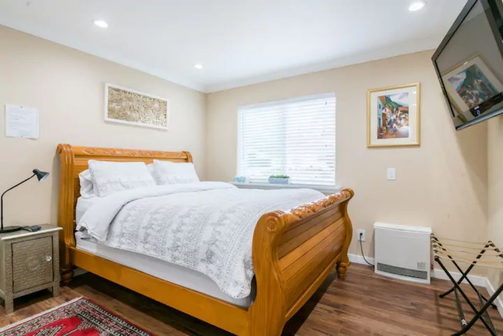 A bedroom with a wooden bed, a nightstand, a radiator, and a window with blinds.