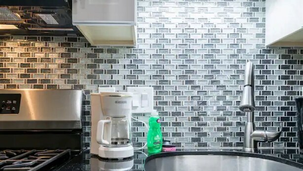 A kitchen with a stainless steel range hood, a coffee maker, and a sink with a modern backsplash.