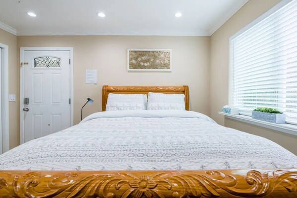 Een slaapkamer met een bed, een deur, een raam met zonwering en een aan de muur hangend kunstwerk.