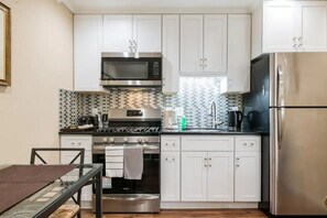 Een kleine keuken met witte kastjes, een RVS magnetron, oven en koelkast.