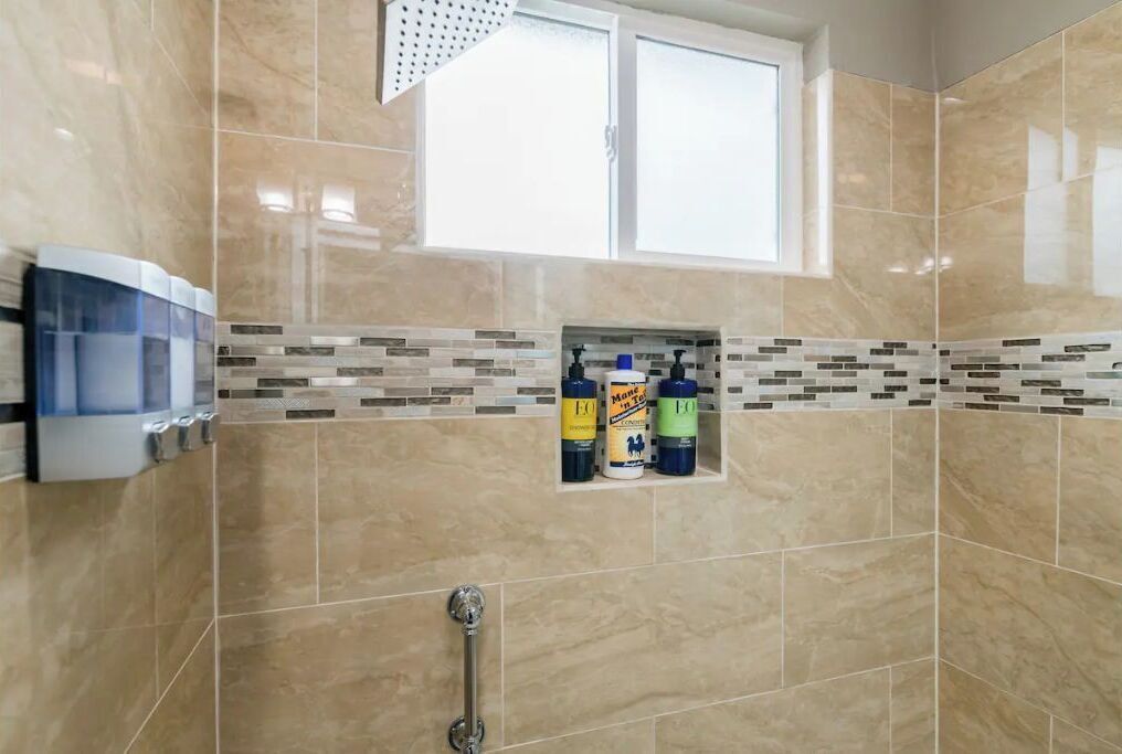Une salle de bain avec des carreaux de couleur beige, une fenêtre et une étagère contenant des produits de nettoyage.