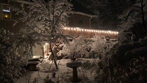 Un jardín cubierto de nieve con una construcción de madera al fondo.