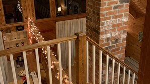 Una escalera de madera con chimenea de ladrillo, barandillas de madera y un ventilador de techo.