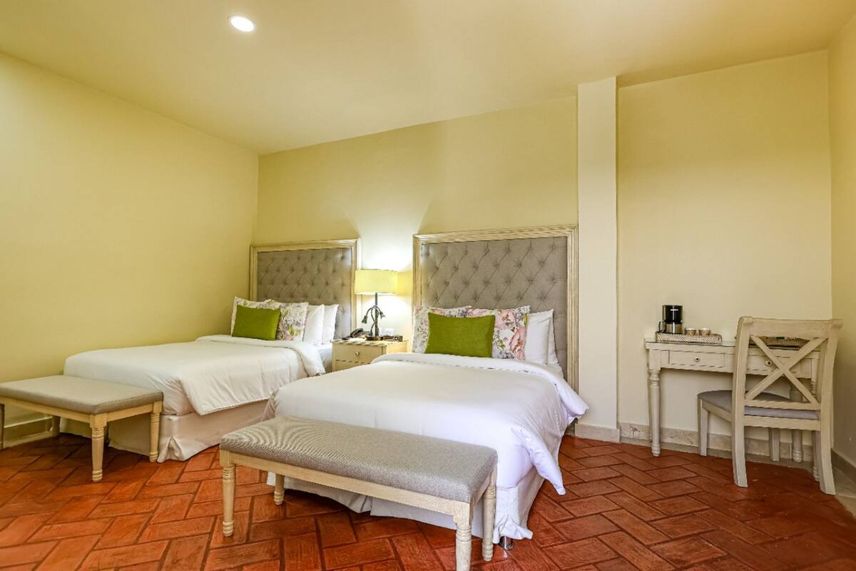 A hotel room with two beds, a bench, a desk, and a chair.
