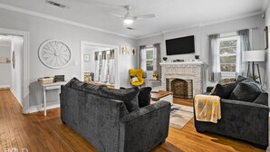 A living room with two grey sofas, a white ceiling fan, a fireplace, and a large wall clock.