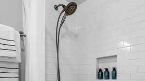 A bathroom with a bathtub, a showerhead, a toilet, and a shelf with toiletries.