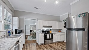 A modern kitchen with white cabinets, a stainless steel refrigerator, and a wooden floor.
