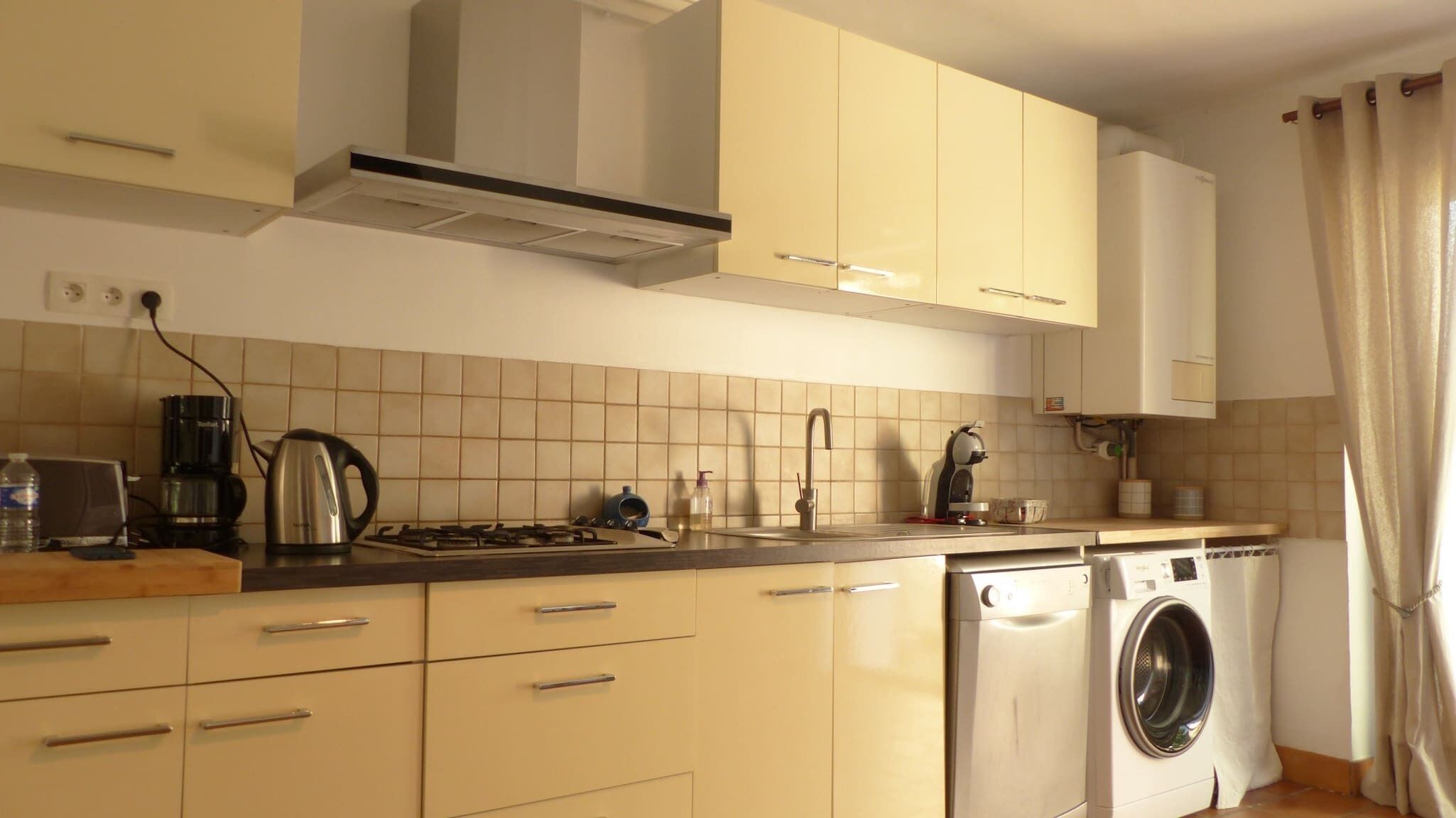 A kitchen with a stove, kettle, coffee maker, and washing machine.