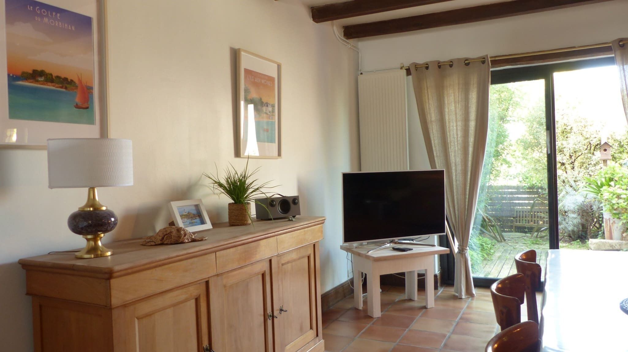 Una sala de estar con televisión, lámpara, planta y un cuadro en un mueble de madera.