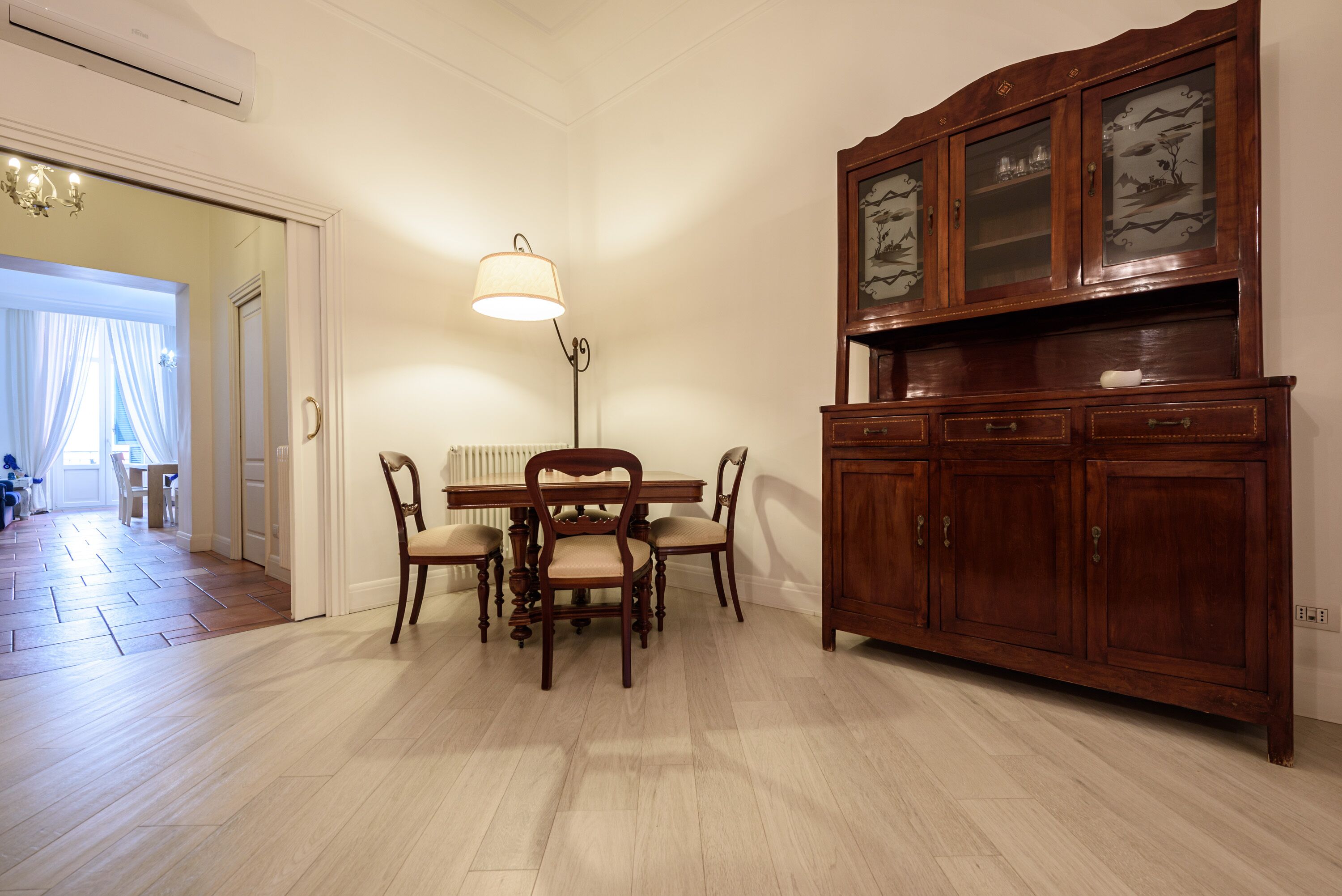 Un comedor con una mesa y sillas de madera, una lámpara y un mueble con puertas de vidrio.