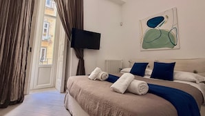 Un dormitorio con cama, televisión, un cuadro y vistas al exterior.