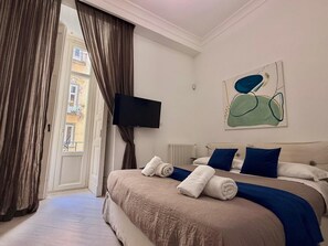 A bedroom with a bed, a TV, a painting, and a view of the outside.
