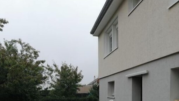 A wooden deck with a white plastic chair, a potted plant, and a building with a white exterior and a window.