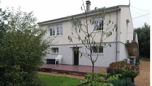 A two-story house with a front porch, a small garden, and a white chair.