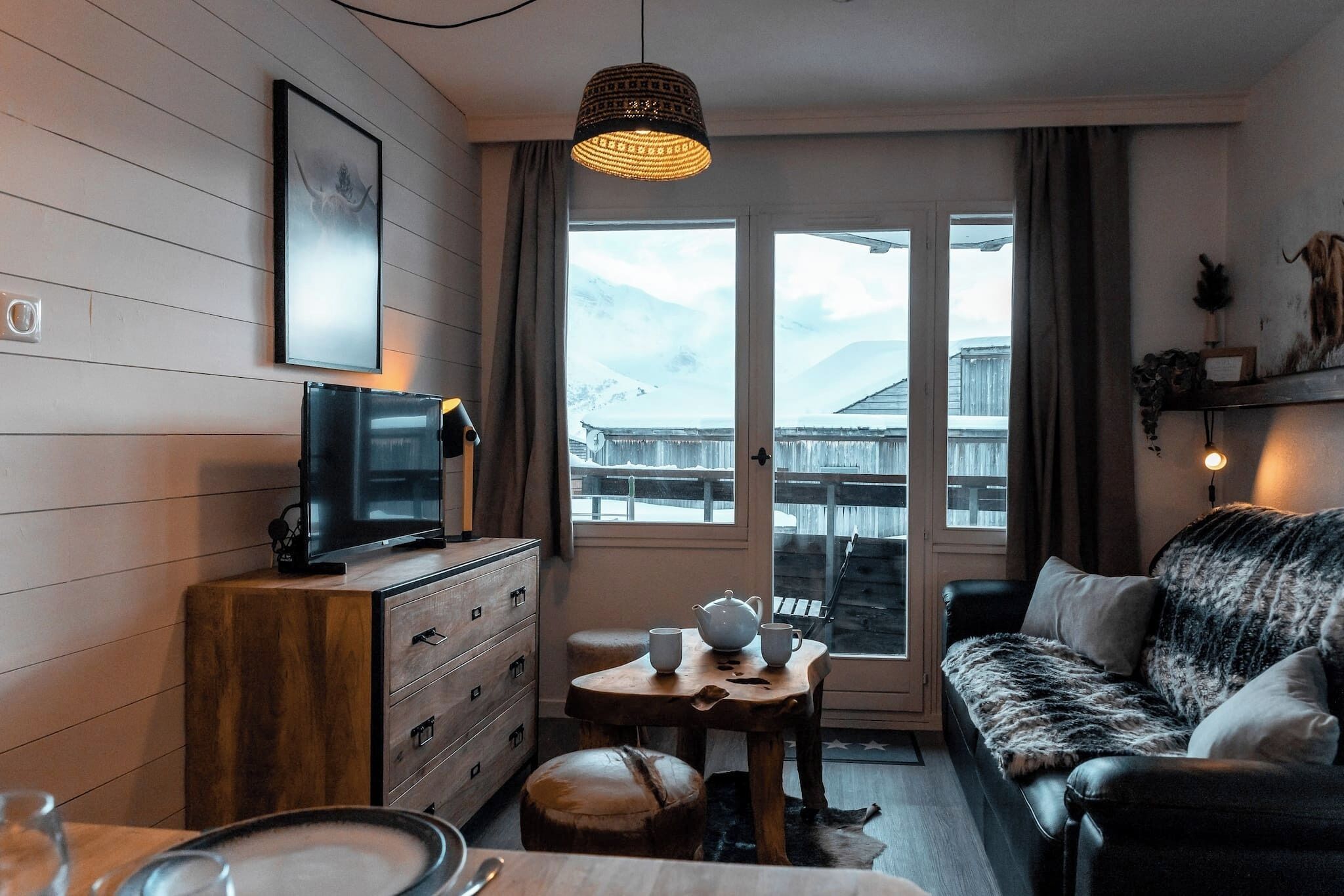 Een knus ingerichte kamer met een houten dressoir, een televisie, een bank en een tafel met kopjes en een theepot.