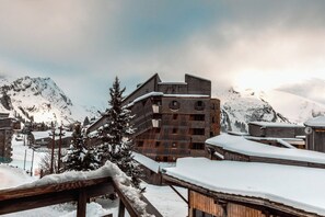 Ein mehrgeschossiges Gebäude mit Holzfassade und geneigtem Dach, umgeben von schneebedeckten Bergen und bewölktem Himmel.