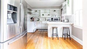 A modern kitchen with stainless steel appliances, white cabinetry, and a wooden floor.