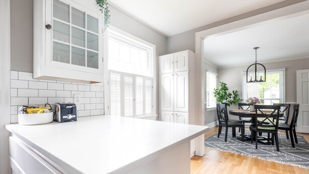 A kitchen with white cabinets, a white countertop, and a dining area with a table and chairs.