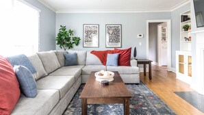 A living room with a sectional sofa, a coffee table, a plant, and framed artwork on the wall.