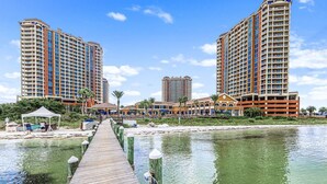 A waterfront hotel with two tall buildings, a boardwalk leading to a beach area, and a clear blue sky.