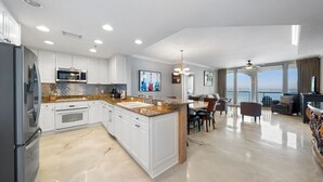 A modern kitchen with white cabinets, granite countertops, and stainless steel appliances. There is a dining area with a large window overlooking a scenic view.
