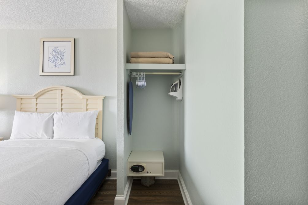 A neatly organized bedroom with a bed, a nightstand, a shelf with folded towels, and a framed picture on the wall.