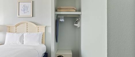 A neatly organized bedroom with a bed, a nightstand, a shelf with folded towels, and a framed picture on the wall.