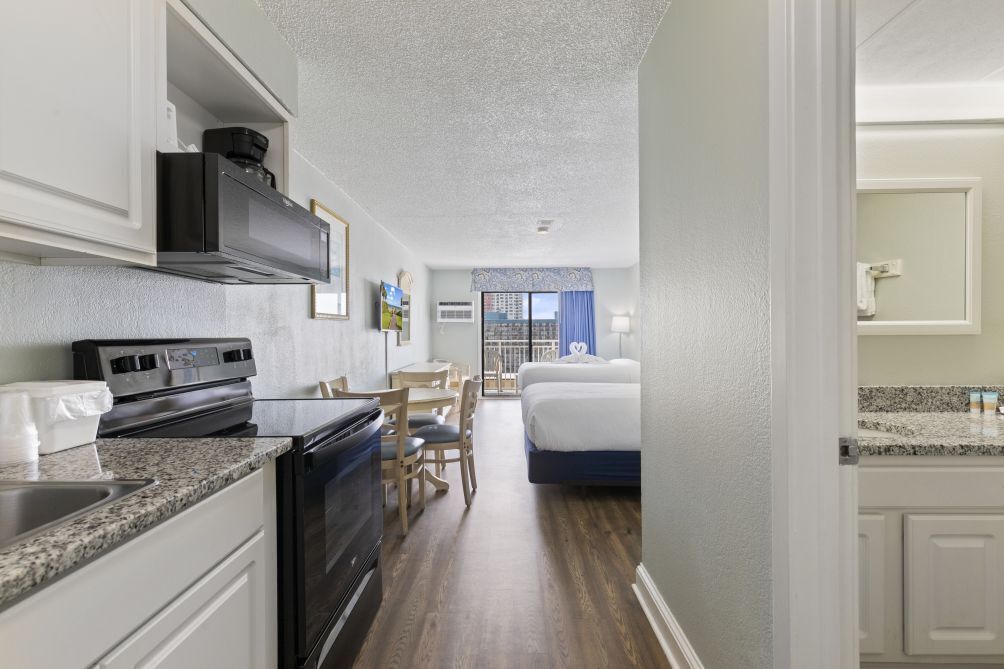 A compact hotel room with a kitchenette, a bed, a small table, and a chair.
