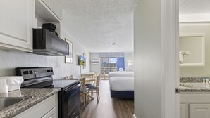 Ett kompakt hotellrum med ett litet pentry, en säng, ett litet bord och en stol.