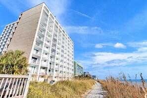 Een hotel met meerdere verdiepingen, balkons, een ligging aan het strand en een heldere lucht.