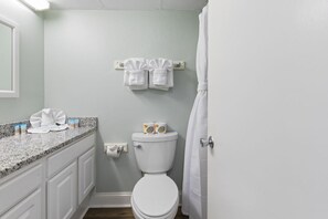 Een badkamer met een wit toilet, een handdoekrek met twee handdoeken, een aanrecht met toiletartikelen en een douchegordijn.