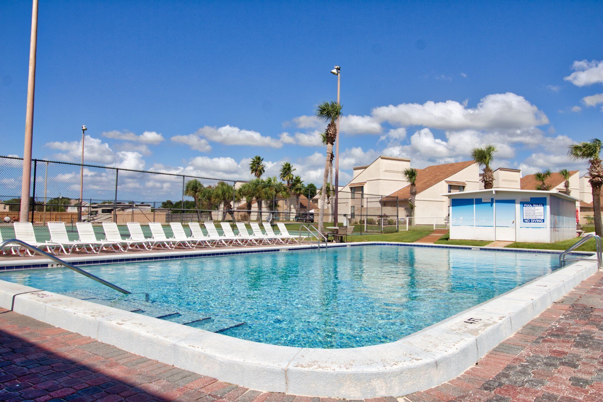 A swimming pool with lounge chairs, a fenced area, and a building with a sign indicating no diving.