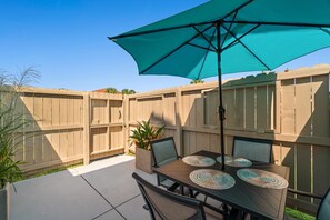 Een buitenpatio met een tafel en stoelen, een grote parasol en een houten omheining.