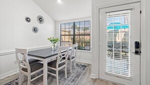 Un coin repas comprenant une table, des chaises et une fenêtre avec des stores.