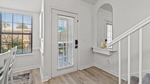 Un intérieur épuré, aux murs blancs, avec un plancher en bois, une porte blanche dotée d’une fenêtre et une petite étagère sur laquelle sont posées des bougies.