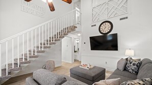Un salon moderne avec un escalier, des canapés gris, un téléviseur à écran plat et un luminaire en bois au plafond.