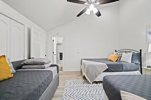 Een slaapkamer met twee bedden, een plafondventilator en een deur die naar een andere kamer leidt.