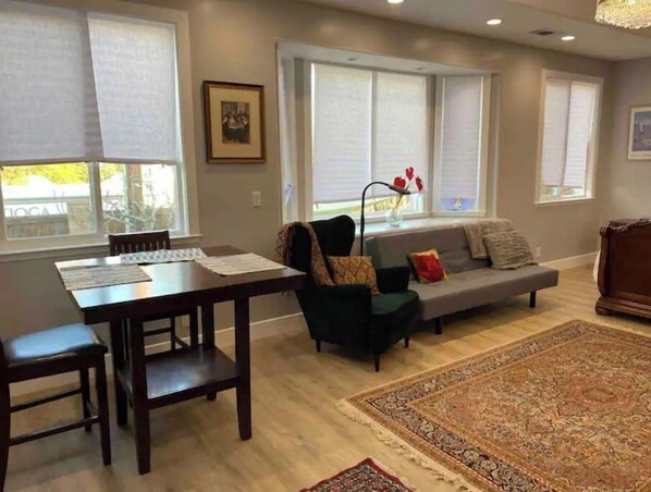 Cozy living area with a dining table for two, comfortable sofa, and large windows.