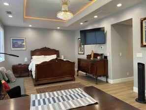Un dormitorio con una cama grande, un aparador, un televisor montado en la pared y una araña.