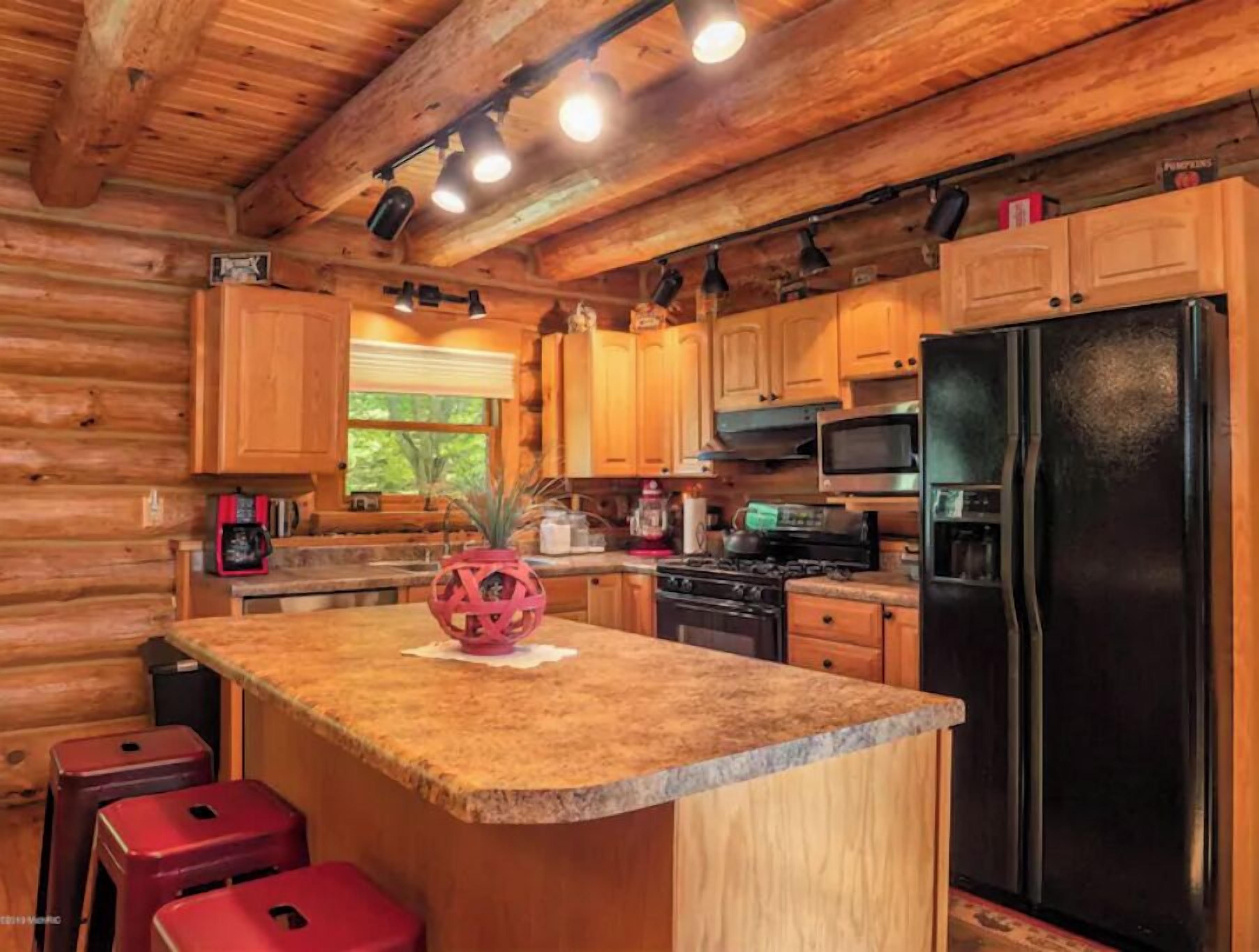 A log cabin kitchen with wooden cabinets, a granite countertop, a black refrigerator, and a coffee maker.