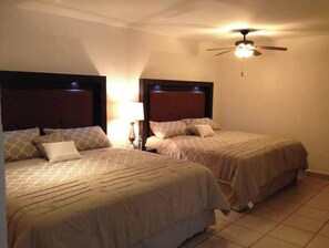 Two single beds with wooden headboards and patterned bedspreads, a ceiling fan, and a wall-mounted light fixture.