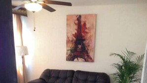 Een woonkamer met een donker leren bank, een schilderij van de Eiffeltoren en rode bloemen op een tafel.